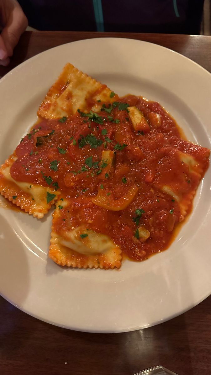 two pieces of ravioli on a white plate with sauce and parmesan cheese