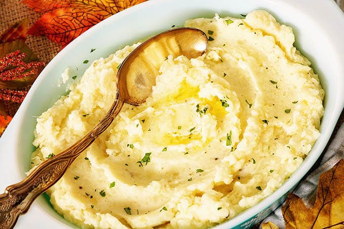 mashed potatoes in a white bowl with a wooden spoon and autumn leaves on the table