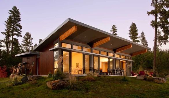 a modern house on top of a hill in the woods at dusk with its lights on