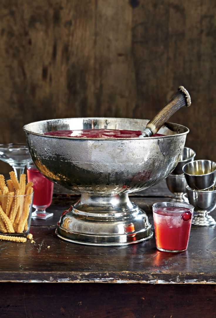 a silver bowl filled with red liquid next to other glasses and food on a table