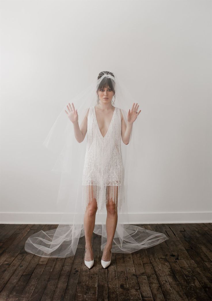 a woman in a white dress and veil standing on a wooden floor with her hands up