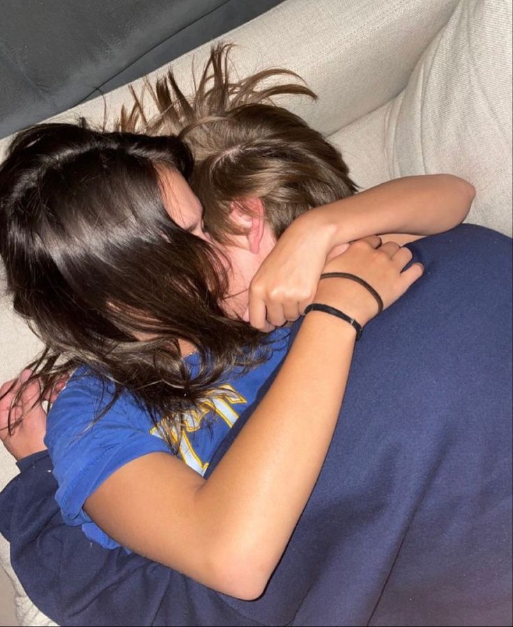 two people laying on a couch hugging each other