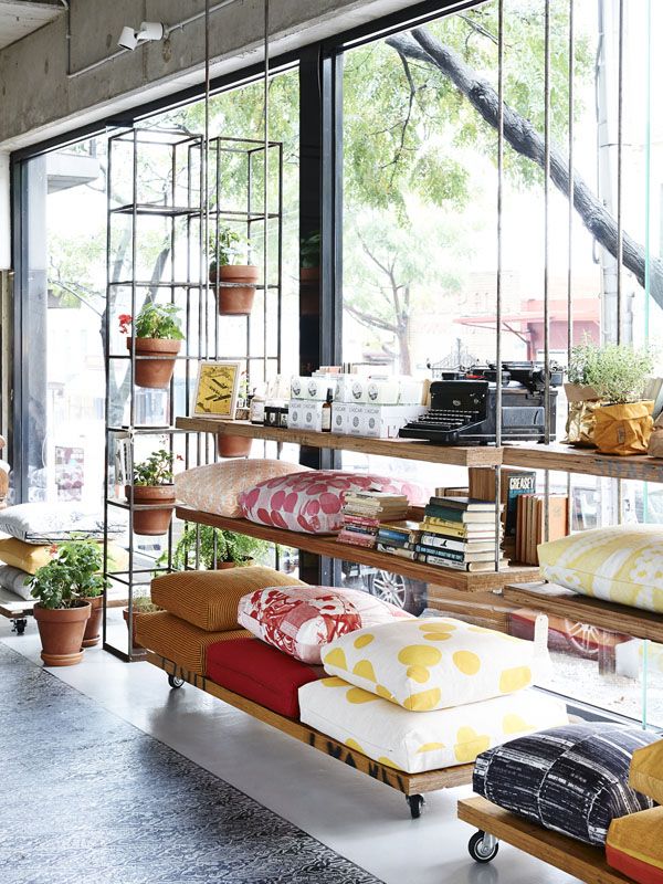 a living room filled with lots of furniture next to a large glass window covered in plants