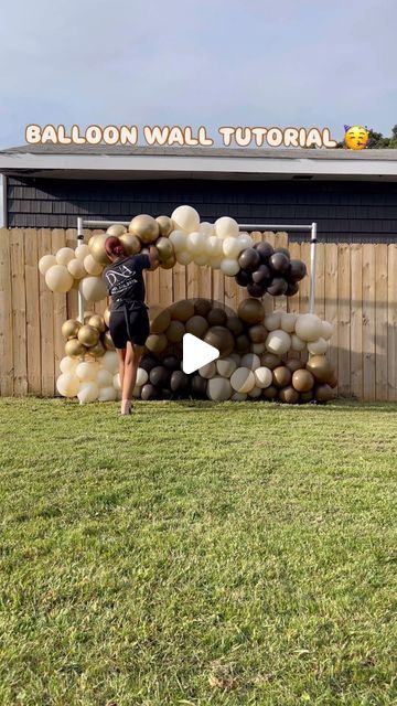 a woman standing in front of a balloon arch made out of rocks and balloons with the words balloon wall