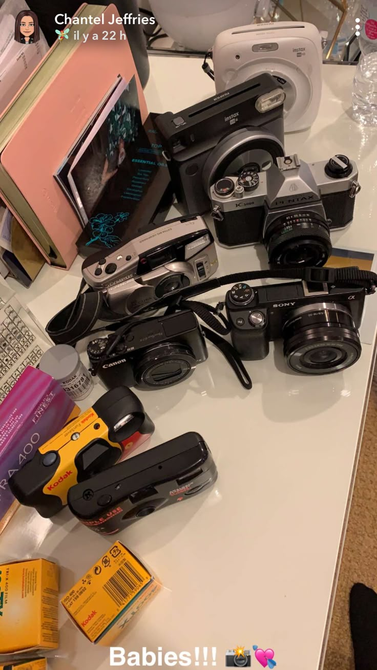 there are many different types of cameras on the table with baby books and other items