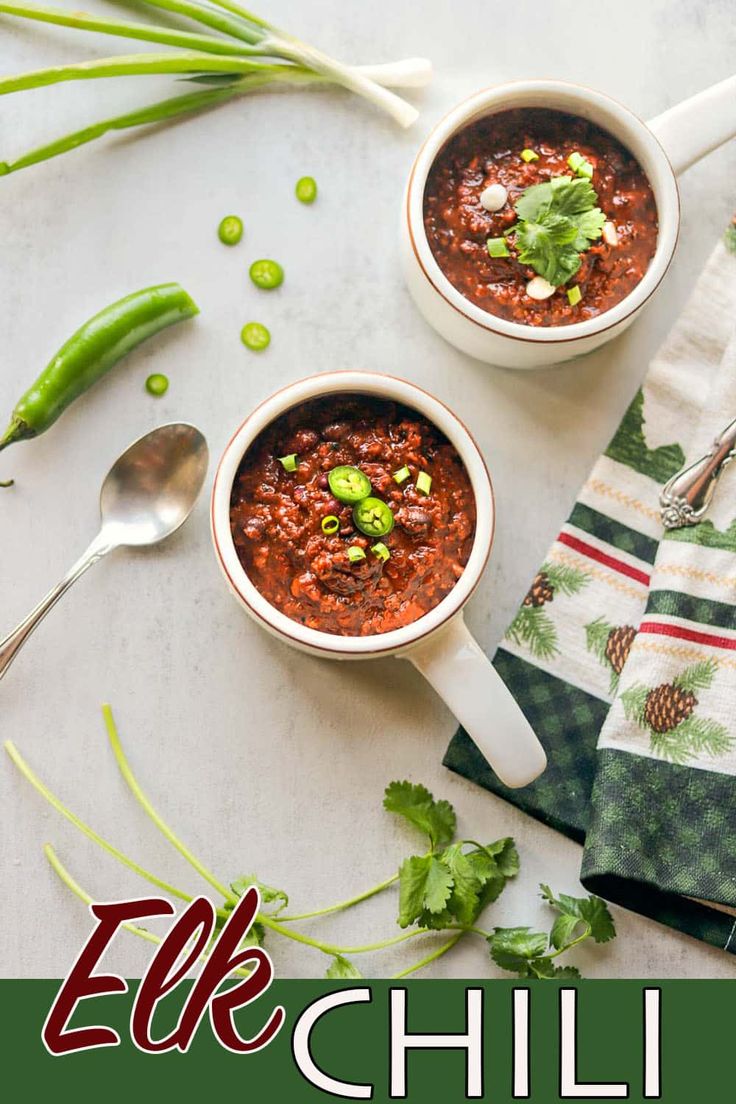 two bowls filled with chili next to spoons and green beans on a tablecloth