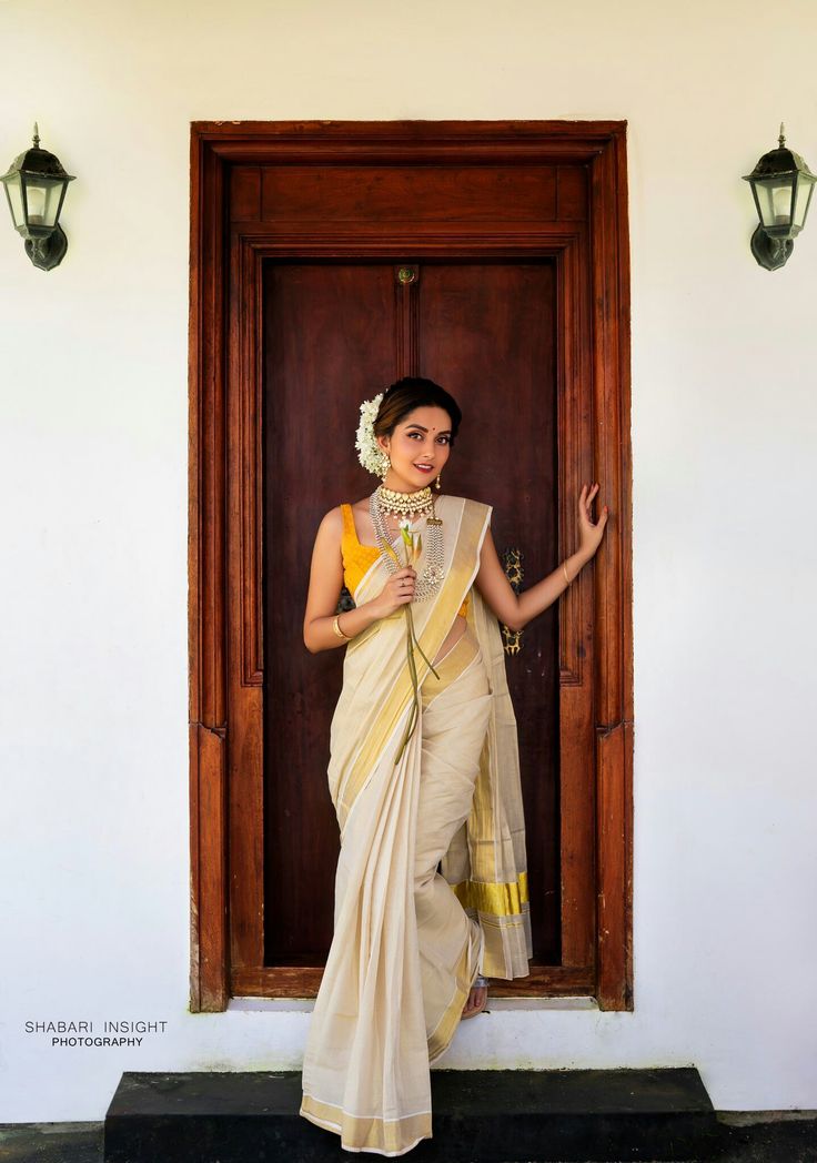 a woman standing in front of a door wearing a white and yellow sari with gold accents