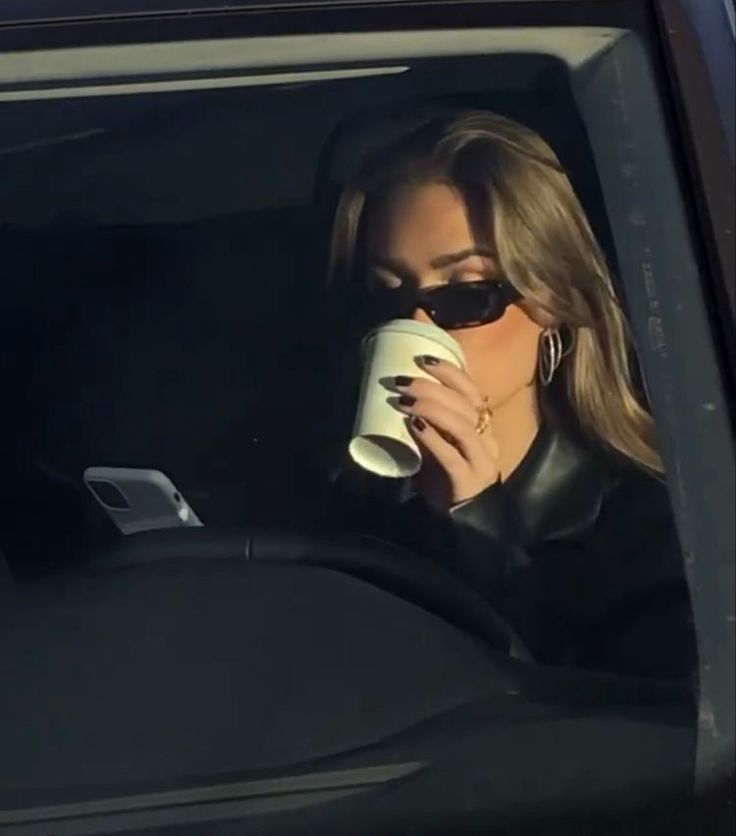 a woman sitting in the back seat of a car drinking out of a coffee cup