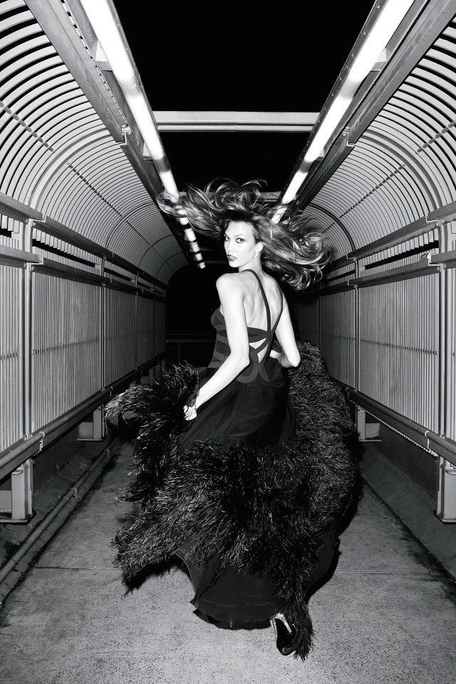 black and white photo of woman in long dress with feathers on the floor inside an airplane