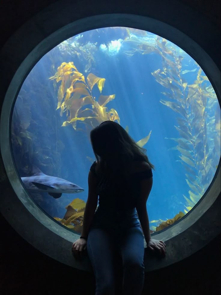 a woman standing in front of an aquarium looking at fish