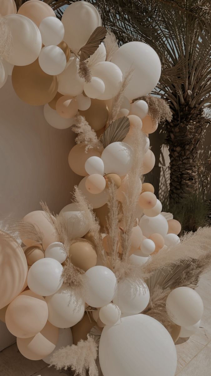 balloons and feathers are hanging from the ceiling in front of a mirror with palm trees behind it