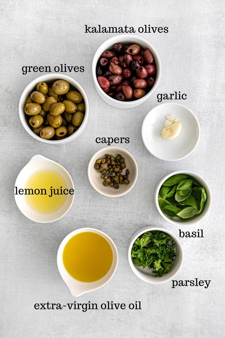 the ingredients for olives are arranged in small bowls on a white surface with green olives, capers, lemon juice, basil oil and parsley