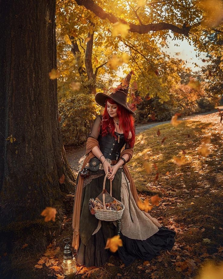 a woman dressed up as a witch sitting under a tree in the fall with her basket