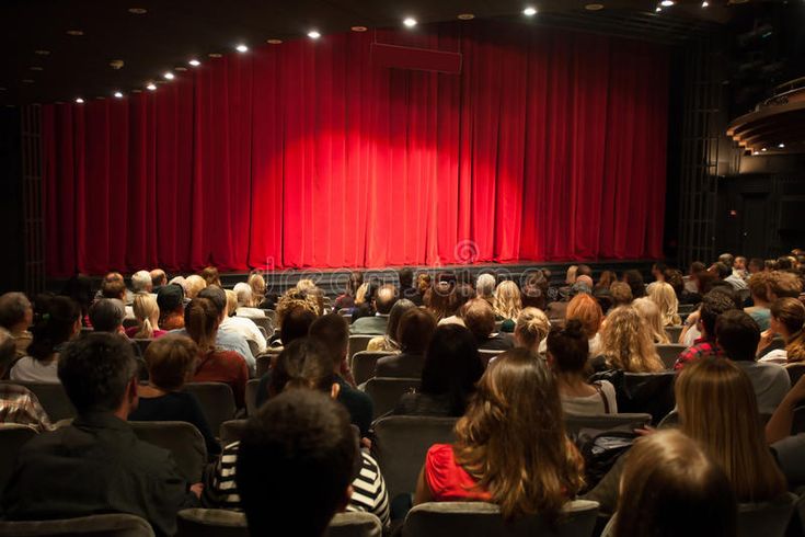 an auditorium full of people with red curtains