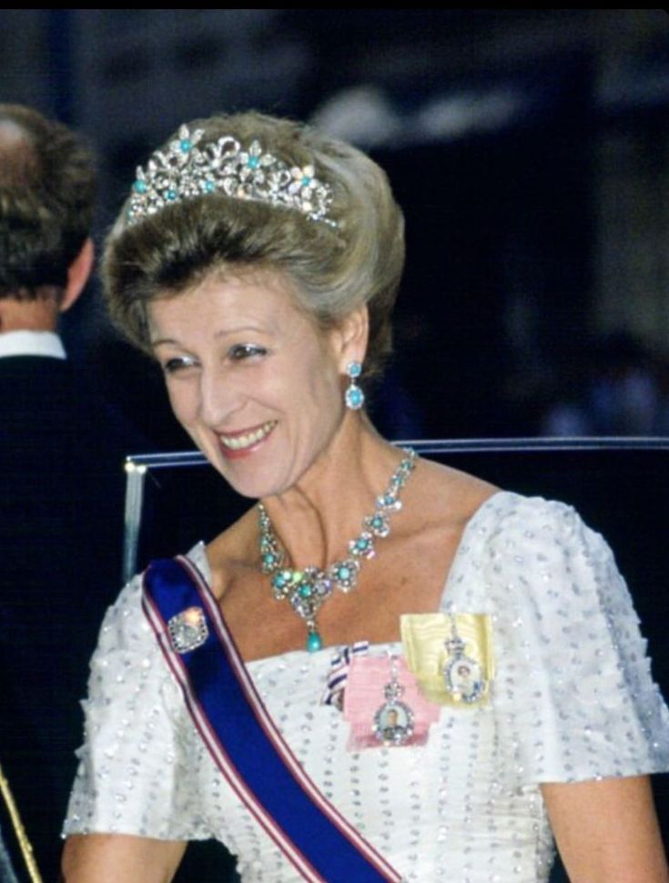 an older woman in a tiara smiles as she sits next to a young man