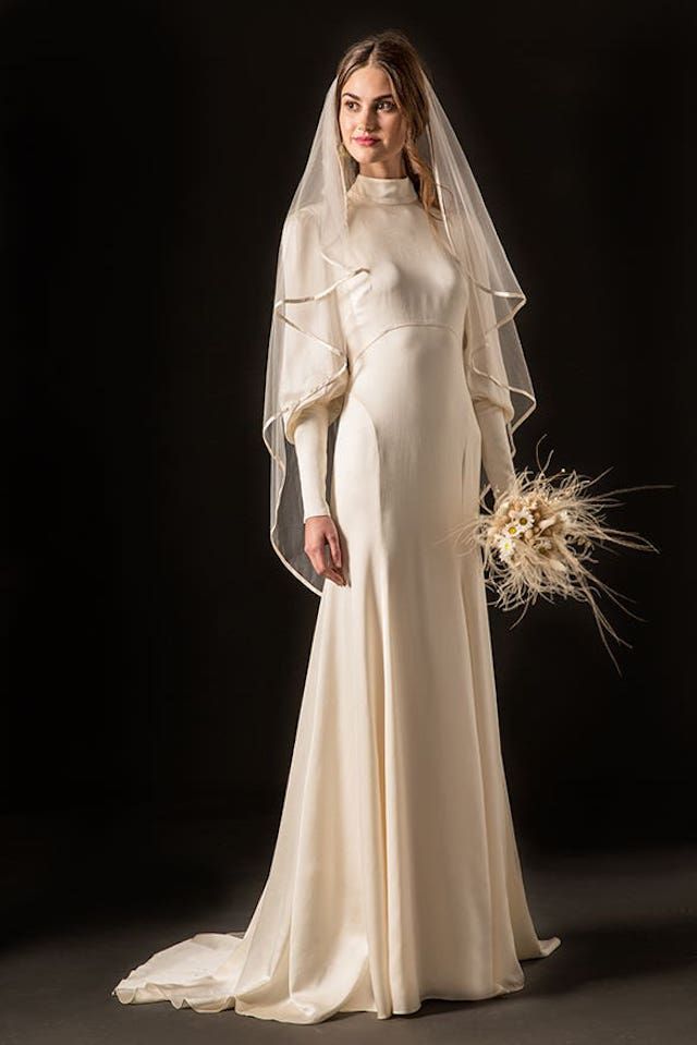 a woman in a wedding dress with a veil on her head and flowers in her hand