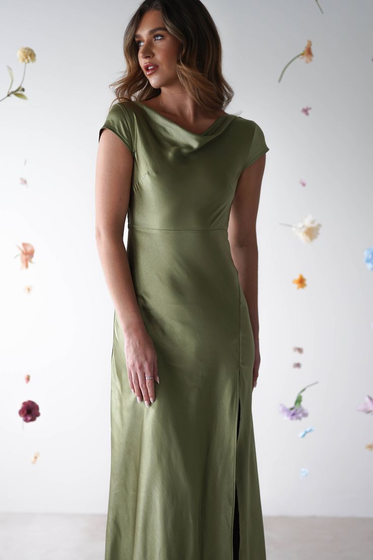 a woman wearing a green dress standing in front of a wall with flowers on it