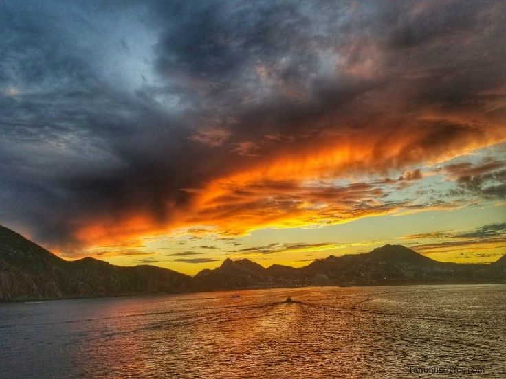 the sun is setting over some mountains in the distance with a boat out on the water