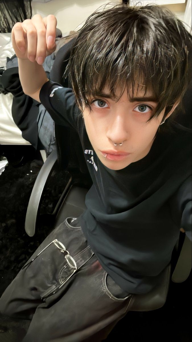 a young man sitting on top of a wooden floor next to a bed and looking at the camera