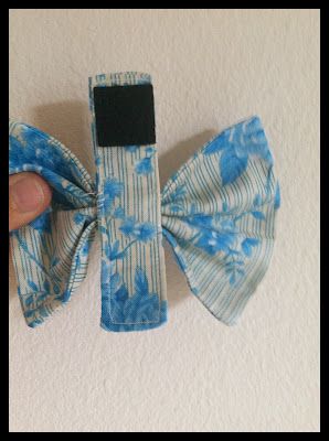 a hand holding a blue and white flowered hair bow on top of a wall