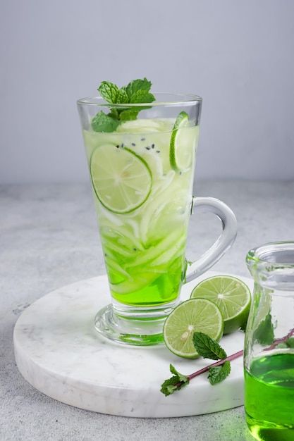 a glass cup filled with green liquid and lime slices next to a jar of lemonade