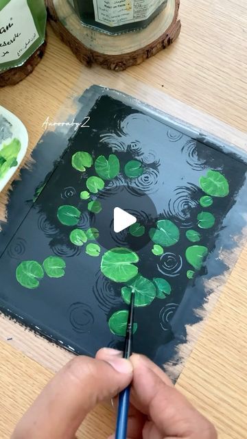 someone is painting water lilies on a piece of wood with green paint and a blue brush