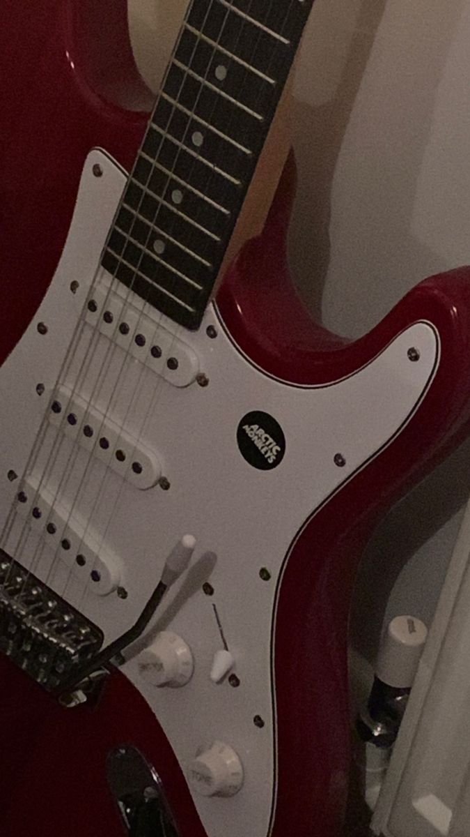 a red electric guitar sitting on top of a table next to a white wall and door