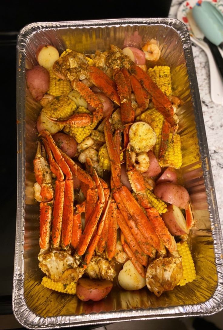 crab legs and corn on the cob in a foil container with potatoes, carrots, and garlic