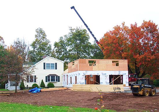 a house under construction with a crane in the foreground and a truck parked on the other side