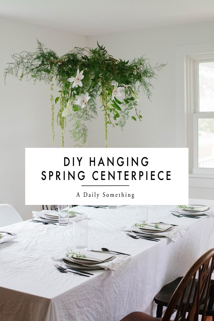 a dining room table set with place settings and greenery hanging from the ceiling above it