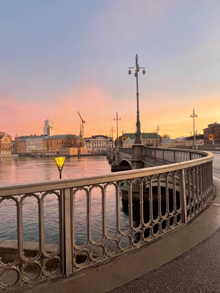 a bridge that is next to the water with buildings in the back ground and a yellow light on it