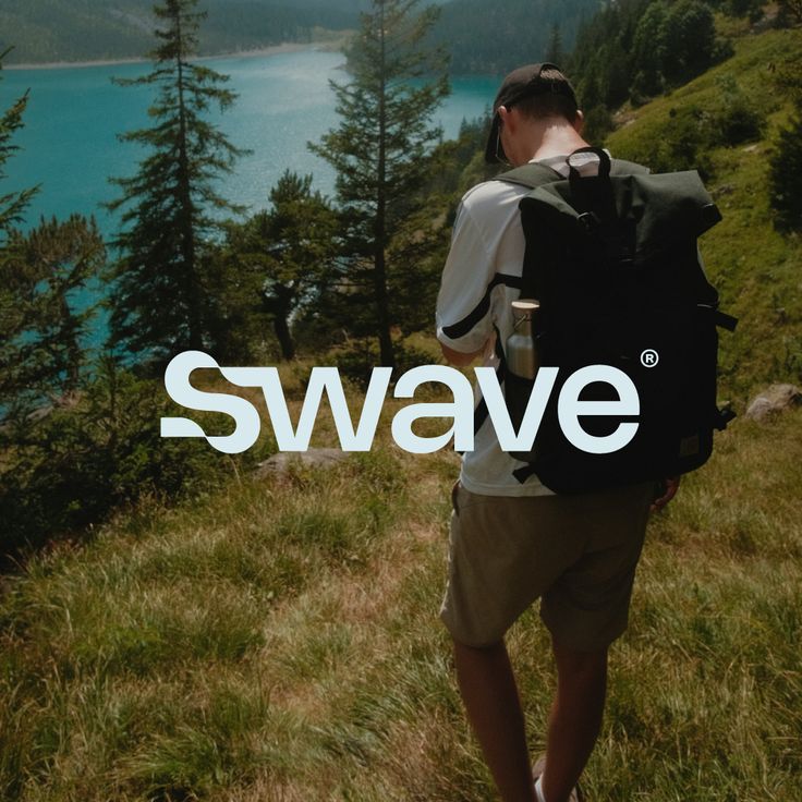 a man standing on top of a lush green hillside next to a lake with the word swave in front of him