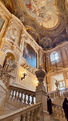 two people are walking up the stairs in an ornately decorated building with paintings on the walls