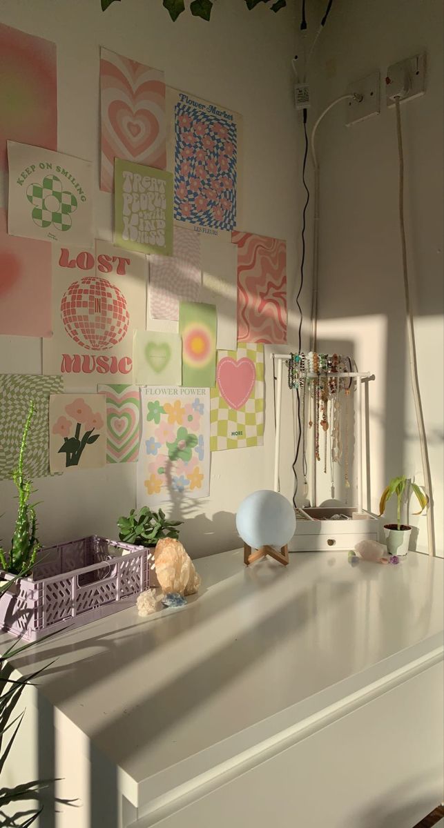 a white desk topped with lots of art on the wall next to a lamp and potted plant