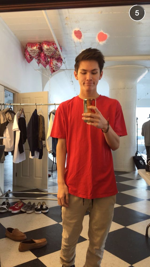 a young man standing in front of a mirror holding a drink and looking at his cell phone