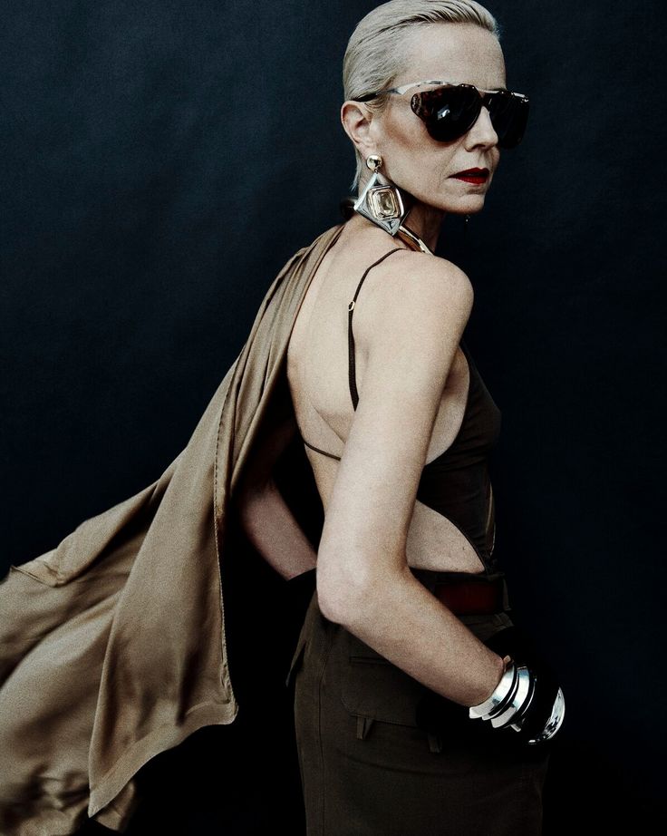 a woman wearing sunglasses and a brown dress is standing in front of a black background