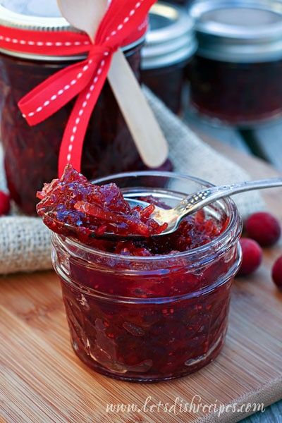 raspberry jam in a jar with a spoon on a cutting board next to it