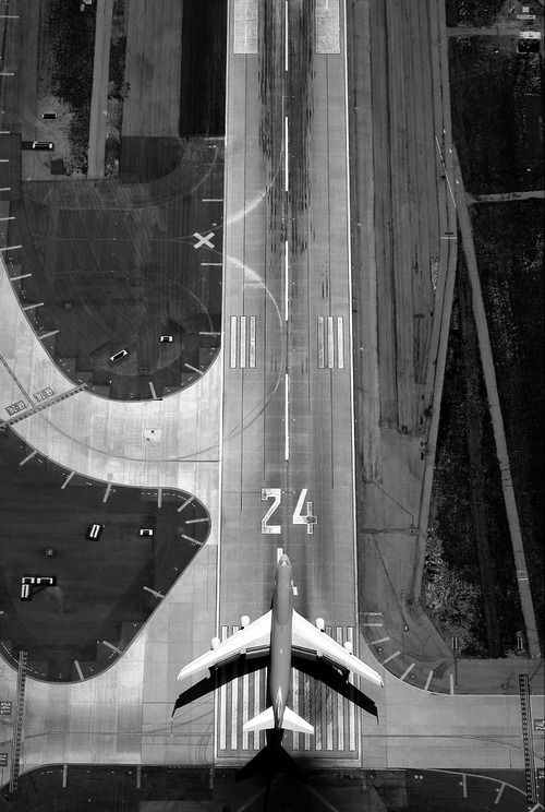 black and white photograph of an airplane flying over the airport with numbers painted on it