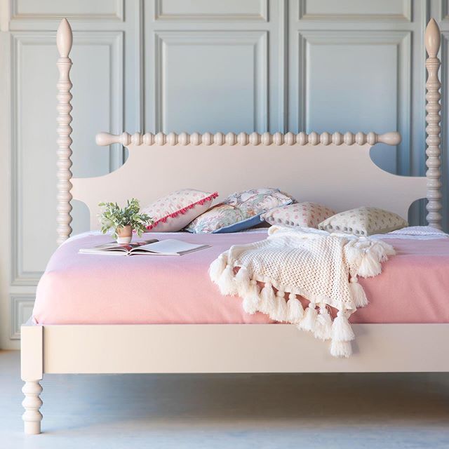 a pink bed with white headboard and foot board, in a room with blue walls