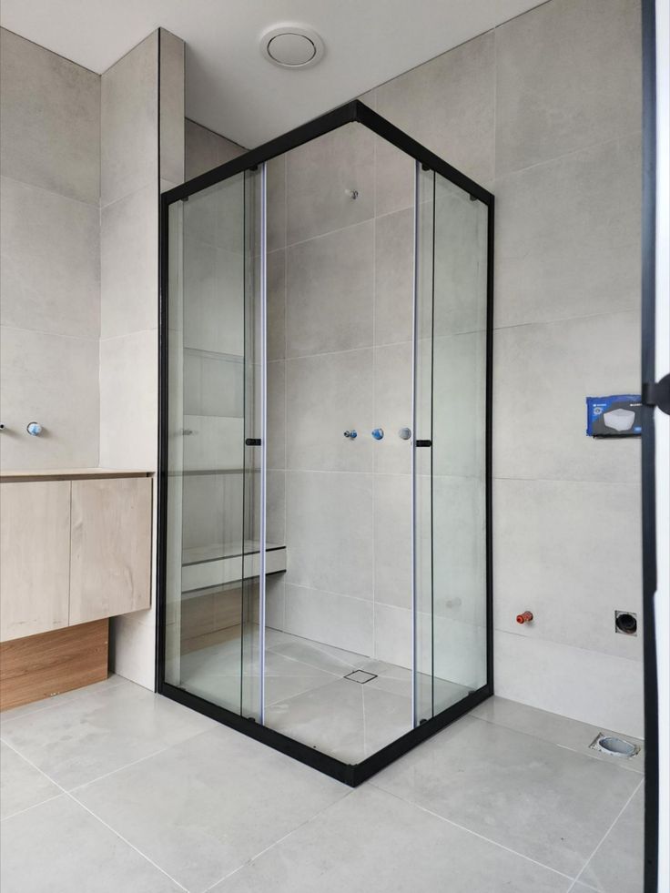 a bathroom with a glass shower stall in the middle and tiled flooring on the other side