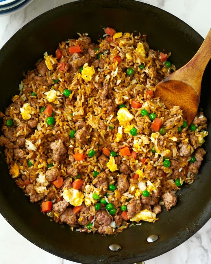 a skillet filled with rice, meat and veggies next to a wooden spoon