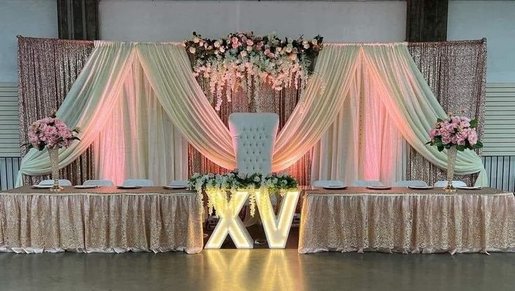 a decorated table with flowers and candles on it in front of a curtained wall