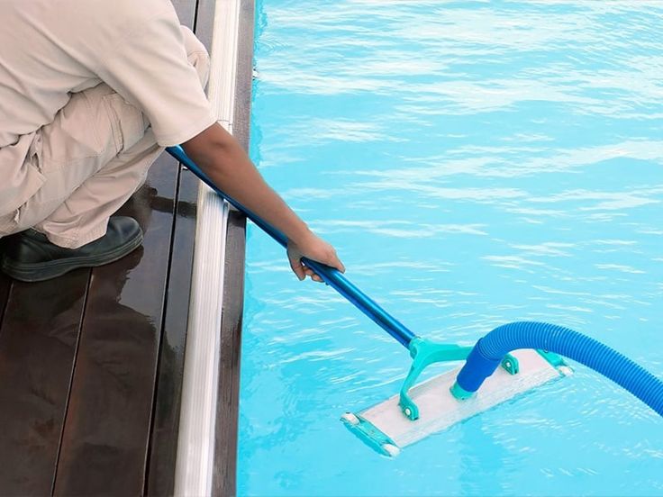 a man is cleaning the side of a swimming pool with a blue and white mop