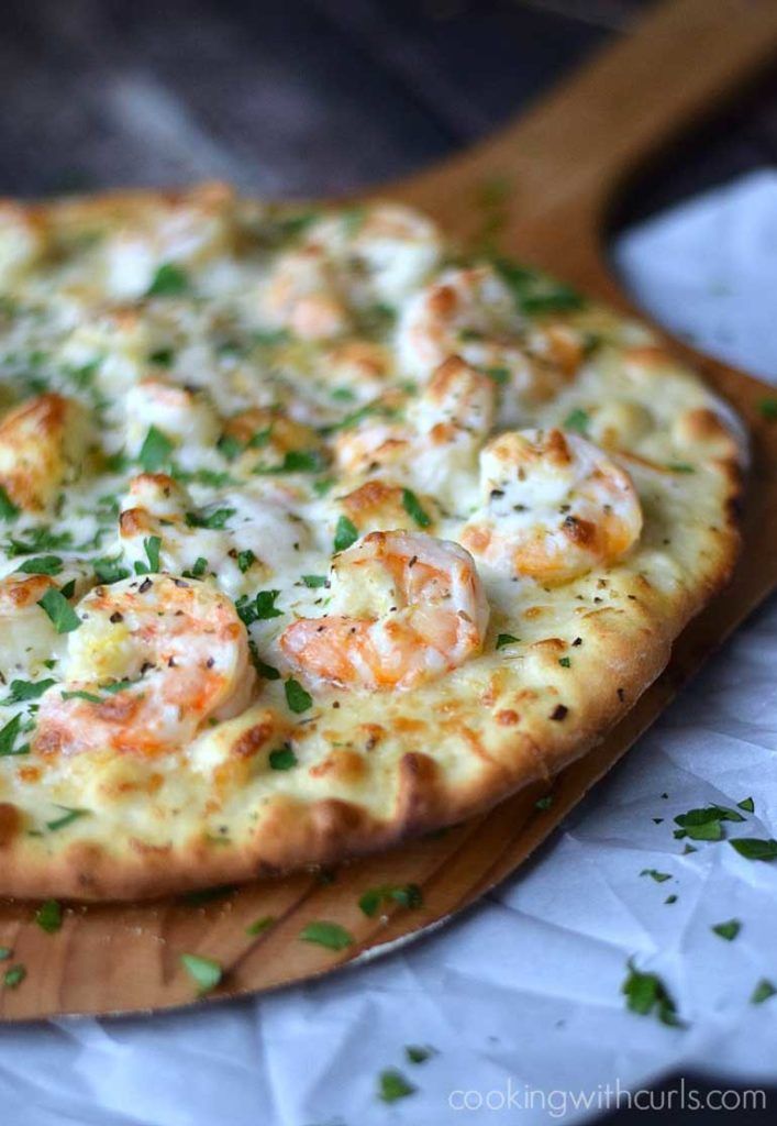 a pizza with shrimp and cheese on a cutting board