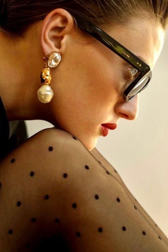 a woman wearing glasses and a pair of pearls on her ear is looking off into the distance