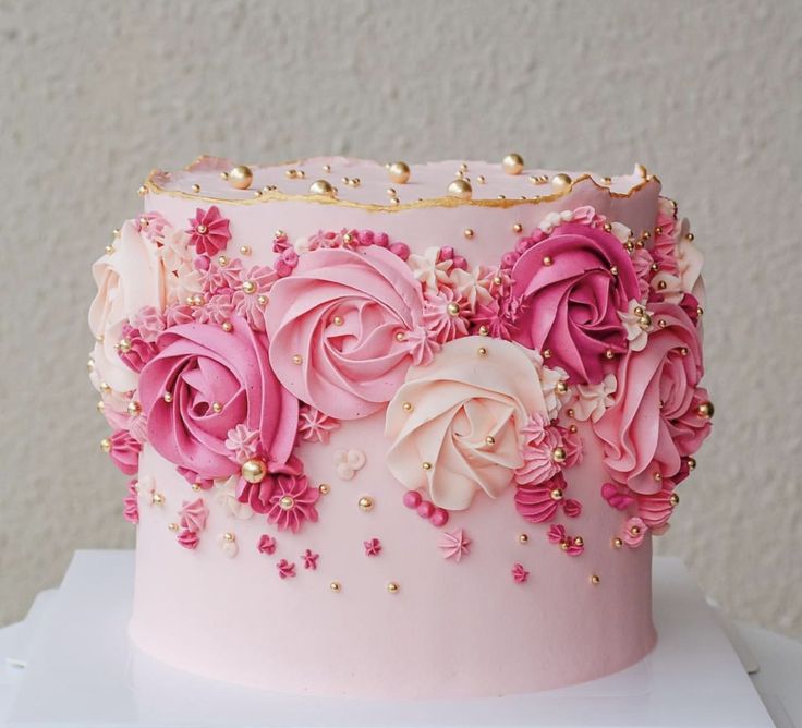 a pink and gold decorated cake with flowers on the top is sitting on a white box