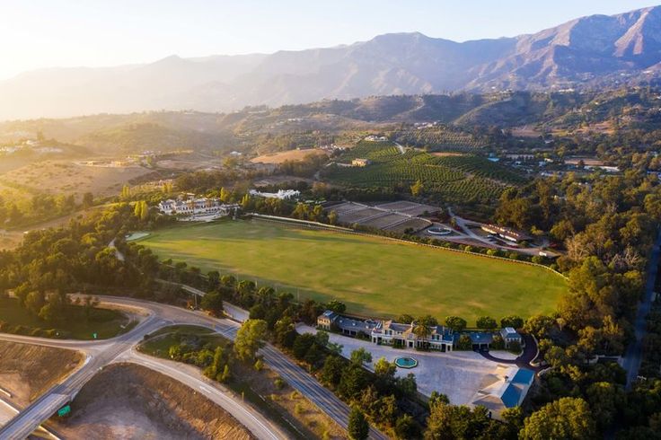 an aerial view of a green field surrounded by mountains