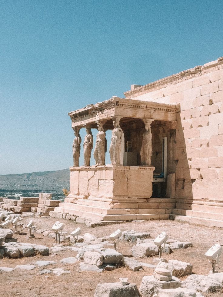 an ancient building with statues in front of it on the side of a mountain range