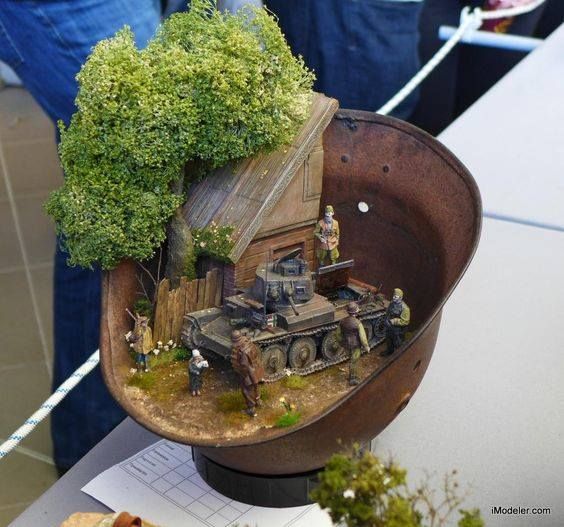 a toy army tank is on display in a bowl with trees and people around it