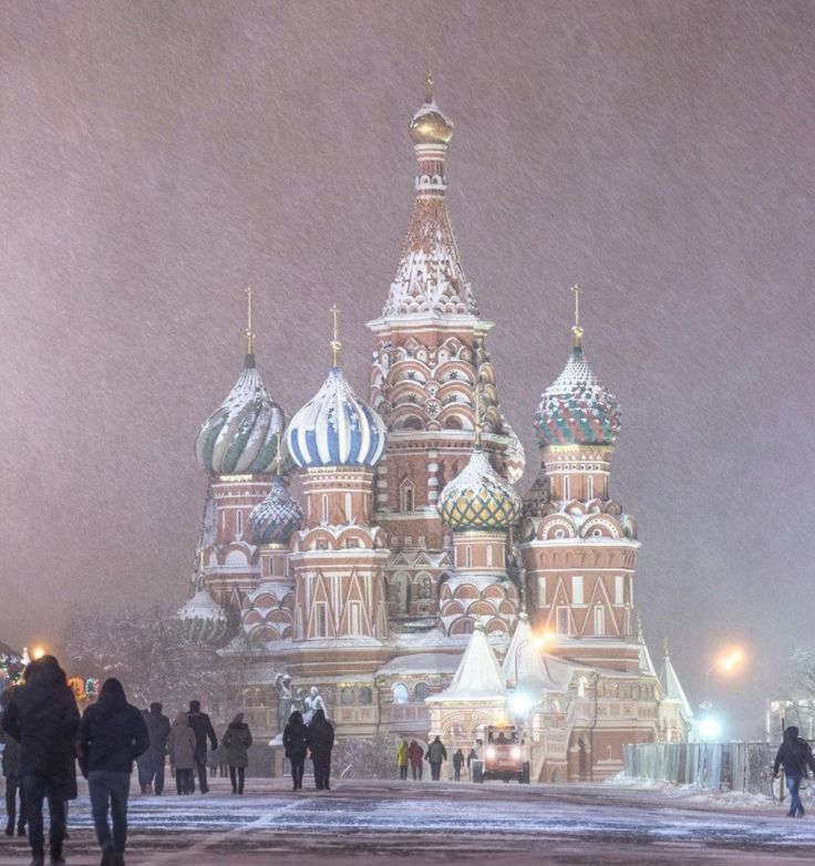 people are walking in the snow near an ornate building that has domes on its sides